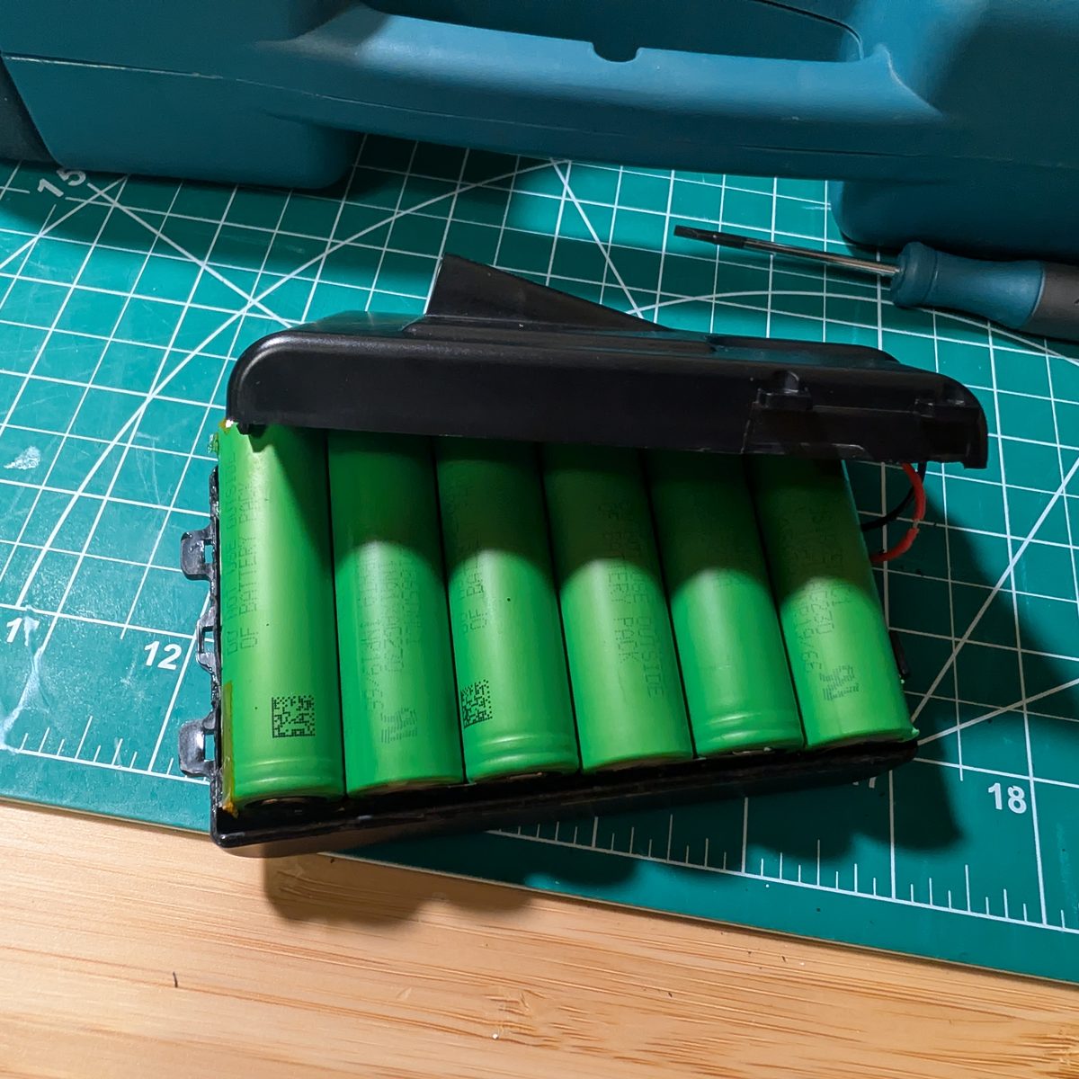Six new brand-name 18650 lithium-ion cells laid out beside an emptied NAO battery housing